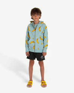 Model wearing Turquoise hoodie with a yellow bananas all-over print. The hoodie has a bronze zipper opening on the front and ribbed cuffs. Made by Nadadelazos
