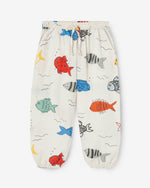 Load image into Gallery viewer, Off-white trousers with a big colourful fish print. The trousers have an elastic waistband with an adjustable cord. It also has two side pockets. Made by Nadadelazos
