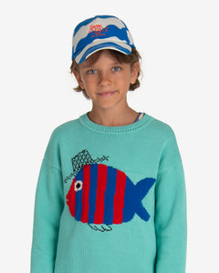 Model wearing Blue and white waves cap with an embroidered detail of a fish and the phrase "Let it Flow" in red. Made by Nadadelazos.